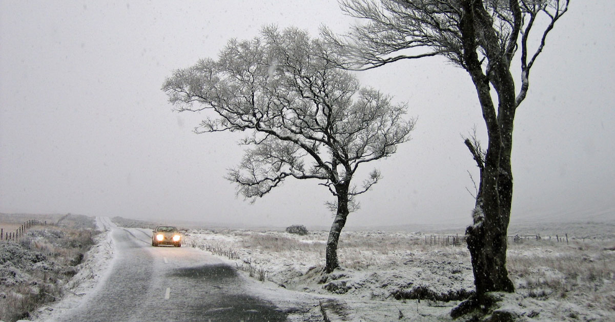 An image of a car driving in the countryside during cold and snowy conditions